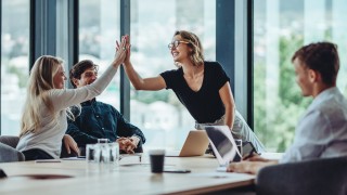 Female professional giving a high five to her colleague in conference room. Group of colleagues celebrating success in a meeting.