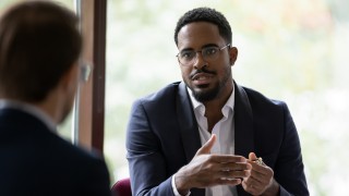 Confident concentrated African American male employee talk with colleague explain thought or idea, focused biracial businessman speak with coworker or partner, brainstorm at office boardroom meeting